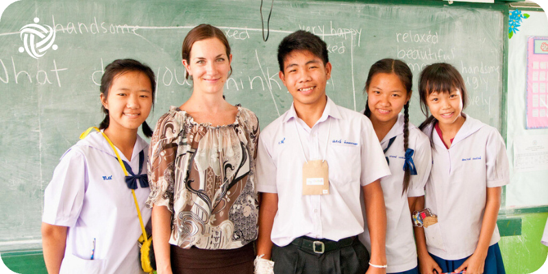 A Teaching Volunteer stand in front of a blackboard in Thailand.
