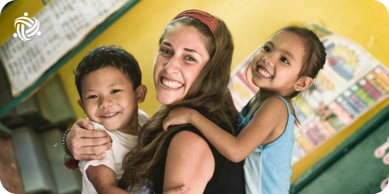 A Woman Volunteering with children in Philippines with two of them in her arms.